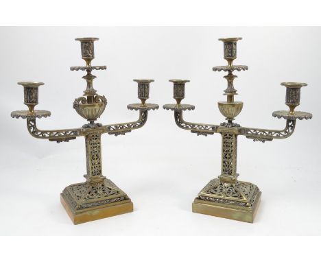 A pair of pierced brass three light candelabra, the middle light supported on an urn column with hairy paw feet, the square s