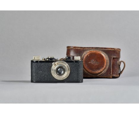 A Leica Elmar camera, circa 1928, ebonised finish, with a Leitz 1:35F 50mm lens and leather carry case. Illustrated. 