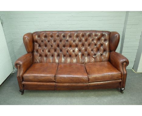 An early 20th century tan leather button upholstered wingback sofa, on squat cabriole supports, 188cm wide x 95cm high.