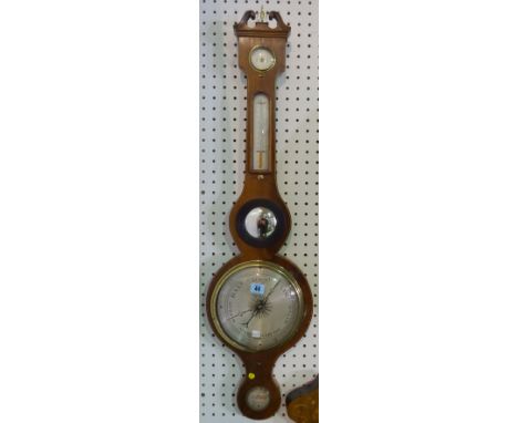 A late 19th century mahogany wheel barometer, with Queen Anne style broken arch pediment over a thermometer, bullseye lens, s