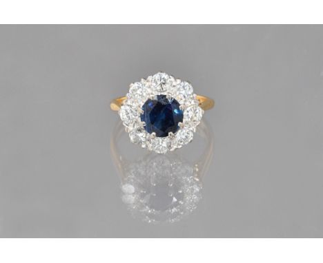An 18ct gold, sapphire and diamond cluster ring, claw set with the circular cut sapphire at the centre, in a surround of eigh
