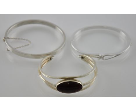 A Sterling silver three band bangle, set with an oval amber-coloured stone, together with a silver hinged bangle, and a white