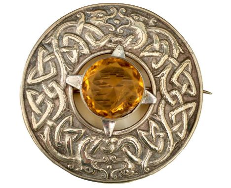 of circular form, the central facetted pale amber coloured stone surrounded by a design of entwined Celtic strapwork and four
