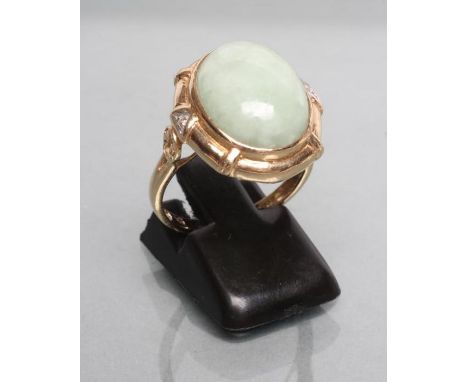 A JADE COCKTAIL RING, the oval cabochon polished stone collet set to a reeded border with a diamond point to each mons pierce