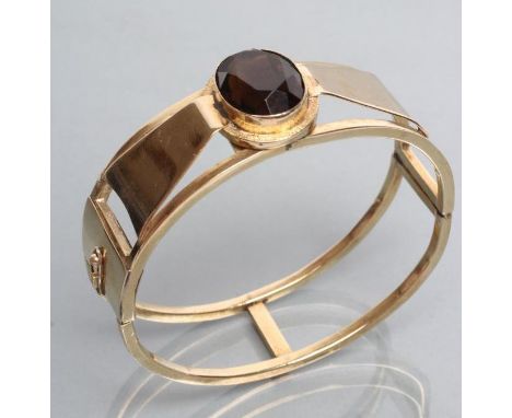 AN AUSTRIAN SMOKEY QUARTZ STIFF HINGED BANGLE, the oval facet cut stone open back collet set to a "bow" within a plain open f