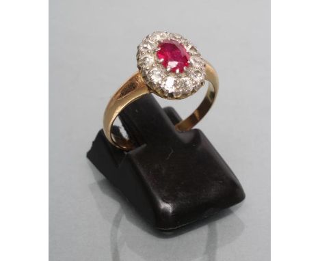 A RUBY AND DIAMOND CLUSTER RING, the oval facet cut ruby claw set to a border of ten round brilliants, wide shoulders and pla