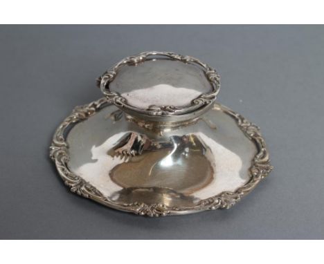 A SILVER CAPSTAN INKWELL, maker's mark HM, Chester 1911, of typical form with cast and applied open scroll rims, 4" diameter,