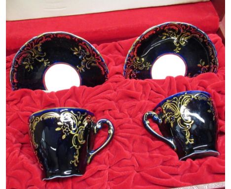 Pair of C20th Royal Dux, Bohemia, cabinet cups and saucers, in fitted case, midnight blue ground with rococo style gilt decor