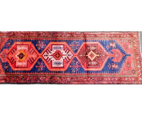 A Persian Hamadan runner, on a red and blue ground, 278cm x 103cm.