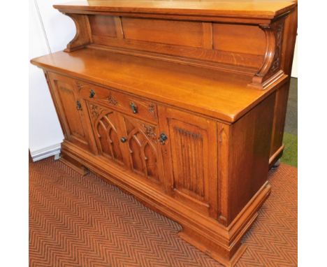 A Continental Gothic oak style sideboard, with a panelled back over a carved frieze drawer above a pair of carved doors, open