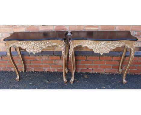 A PAIR OF MODERN CARVED WOOD CONSOLE TABLES having fancy shaped black painted tops, carved &amp; limed apron supported on fou