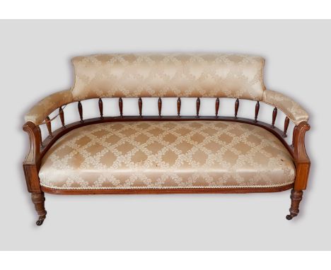 A late Victorian walnut sofa, the upholstered and spindle back above a stuff over seat raised upon turned tapering legs 