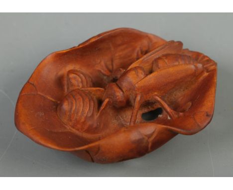 A hand carved hardwood netsuke of a bee on lotus  