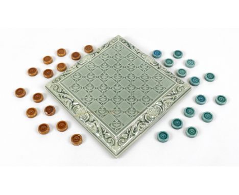 An Art Nouveau pottery draughts board and draughts, by Leeds Fireclay Co. Ltd , the square board decorated in a pale green gl