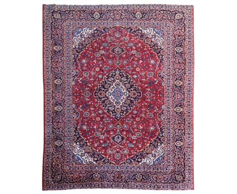 Large Kashan crimson ground carpet, central indigo medallion with stylised floral motifs, flanked by matching spandrels, bord