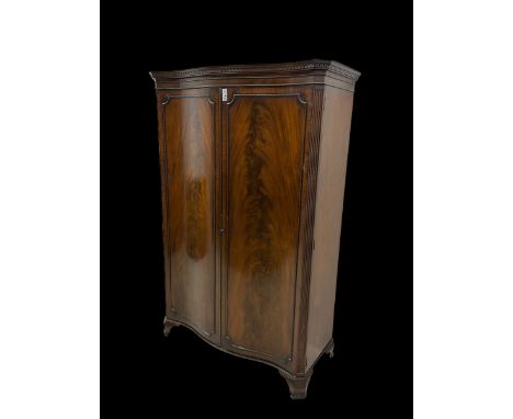 Early 20th century mahogany serpentine double wardrobe, moulded cornice over two figured doors, the interior fitted with hang