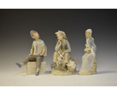 Two Lladro porcelain figures, girl with doll (5400) seated girl holding lilies, and a Nao figure of a young newspaper seller 