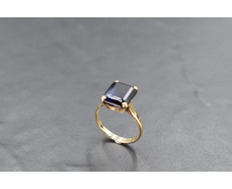 A 9ct gold and blue stone dress ring, the emerald-cut claw-set between shaped and pierced shoulders, the shank marked 9ct, ri