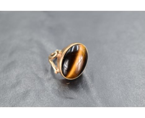 An oval tigers eye cabouchon stone ring having a diagonal set collared mount to open shoulders on a 9ct gold loop, size E 7 a