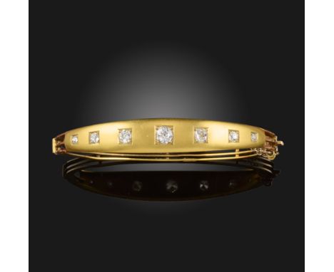 An Edwardian gold hinged bangle, set with seven graduated old circular-cut diamonds and with scroll engraved shoulders, inter