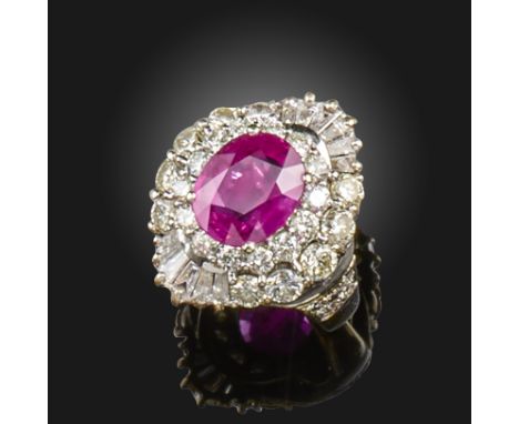 A ruby and diamond cluster ring, the oval-shaped ruby is set within a surround of round brilliant-cut diamonds, with further 