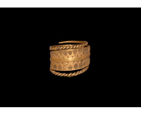 9th-12th century AD. A gold ring formed of a flat band tapering to a point at each end; wide centre decorated with a series o