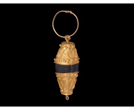 10th-12th century AD. A pendant comprising a fusiform glass bead with sheet gold cap to each end, each cap with applied filig