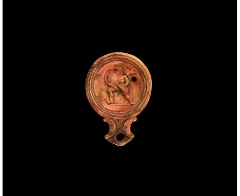 1st century BC-1st century AD. A ceramic oil lamp with angled nozzle and pelta motif to the side; dished top decorated to the