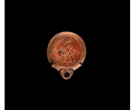 2nd-3rd century AD. A ceramic oil lamp with broad body and short D-shaped nozzle, ribbed shoulder and low-relief image of a s