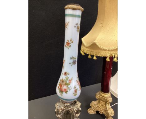 A late Victorian hand painted milk glass lamp stand, silver metal baroque style base, 62cm high; a ruby glass table lamp with