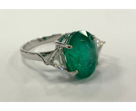 An emerald and diamond ring, central oval emerald approx 5.63ct, between trilliant cut diamond shoulders, total diamond weigh