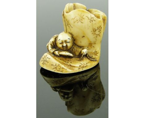 A late 19th century carved ivory netsuke
depicting a man holding a rope climbing on a boot, signed, height 1.2".