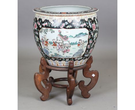 A 20th century Chinese porcelain jardinière on a shaped hardwood stand, the bowl decorated with figures at leisure against a 