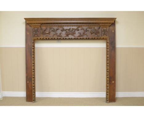 An 18th Century style pine Fire Surround with dentil frieze, floral and scroll carved panel, 5ft 8in wide, labelled Keeble, C