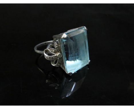 A white gold ring set with a large aquamarine, 2cm x 1.5cm with diamond studded "bow" shoulders, stamped 18ct, shaft bent, 12