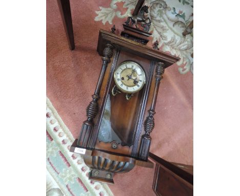 An early 20th century stained frame Vienna wall clock having horse finial, half pillars and glass trunk enclosing circular ro