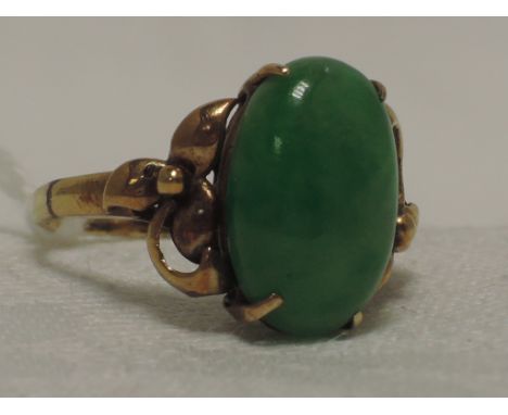 A ladies dress ring having an oval jade cabouchon stone in a  claw setting to moulded shoulders on a yellow metal loop, marks