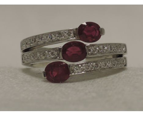 A ladies dress ring having a triple row of diamonds with central oval ruby and ruby terminals to outer rows on a white metal 