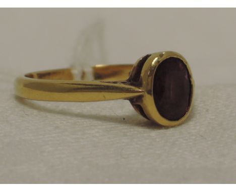 A ladies dress ring having an oval ruby in a plain collared mount to raised shoulders on an 18ct gold loop,  approx 3.3g