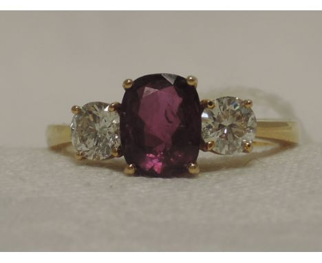 A ladies dress ring having an oval ruby flanked by two brilliant cut diamonds, each approx .5ct in a raised claw setting on a