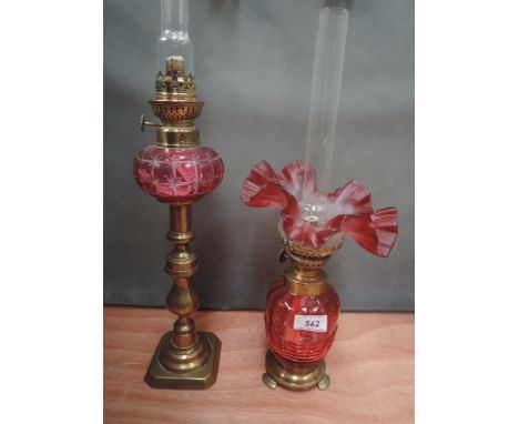 A cranberry glass and brass oil lamp having fluted shade and a cranberry glass oil lamp on brass candlestick base