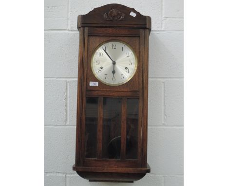 An early 20th century oak wall clock having silvered circular dial and glass trunk