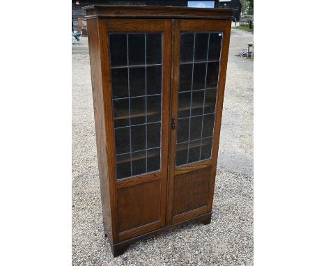 An oak&nbsp; bookcase with leaded part-glazed and panelled doors enclosing fixed shelves, raised on bracket feet, 169 cm high