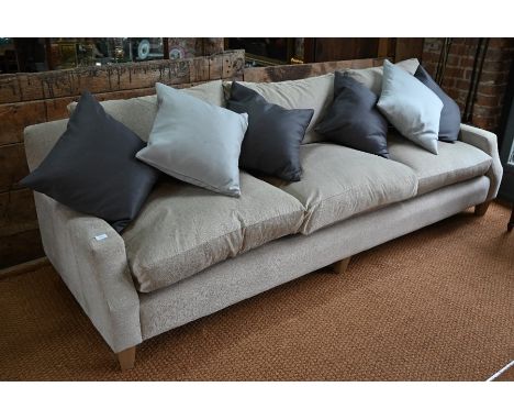 A contemporary three seater sofa with feathered filled cushions in oatmeal fabric upholstery, with straight back and tapered 