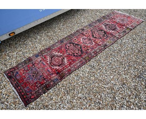 A Persian Hamadan runner with geometric medallions and stylised floral design on red ground, 310 x 85 cm