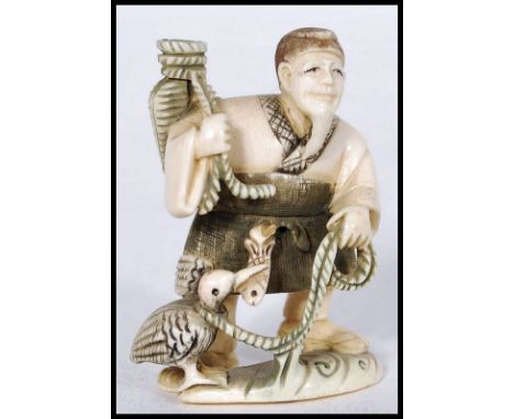 A Japanese Meiji Period ivory netsuke carved as a fisherman with basket over his shoulder and cormorant at his feet with fish