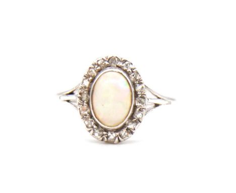 An opal and diamond cluster ring, the oval cabochon cut opal collet set and surrounded by sixteen rose cut diamonds in an all