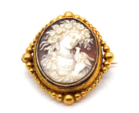 An oval carved shell cameo brooch in yellow metal mount, female profile to the right holding a bird, engraved unmarked yellow