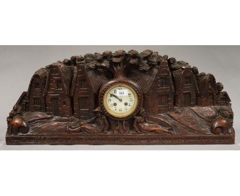 FOLK ART. A FRENCH CARVED OAK MANTEL CLOCK IN THE FORM OF A VILLAGE SCENE, WITH THE SEATED FIGURES OF A MAN AND WOMAN EITHER 