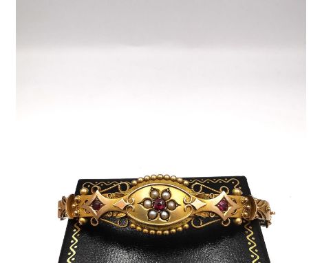 An Edwardian 9ct rose gold ruby and seed pearl bracelet with beaded detailing and wire work scrolling, set with three round m
